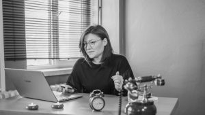 A businesswoman using a laptop at her desk with a vintage phone and an alarm clock, creating a mix of modern and retro vibes.