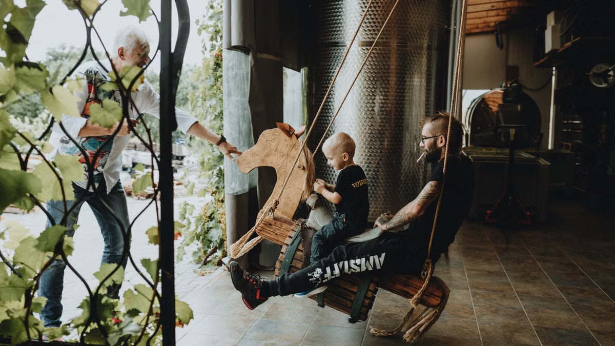 A father and his child enjoy a playful moment on an indoor wooden swing in a rustic setting.